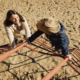 Frau mit Kind am Spielplatz. Kind auf Klettergerüst und blickt nach unten zu ihrer Mutter. Diese blickt nach oben.